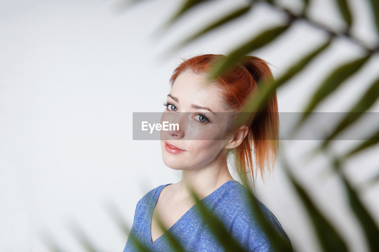 Indoor portrait of young woman shot through plant leaves