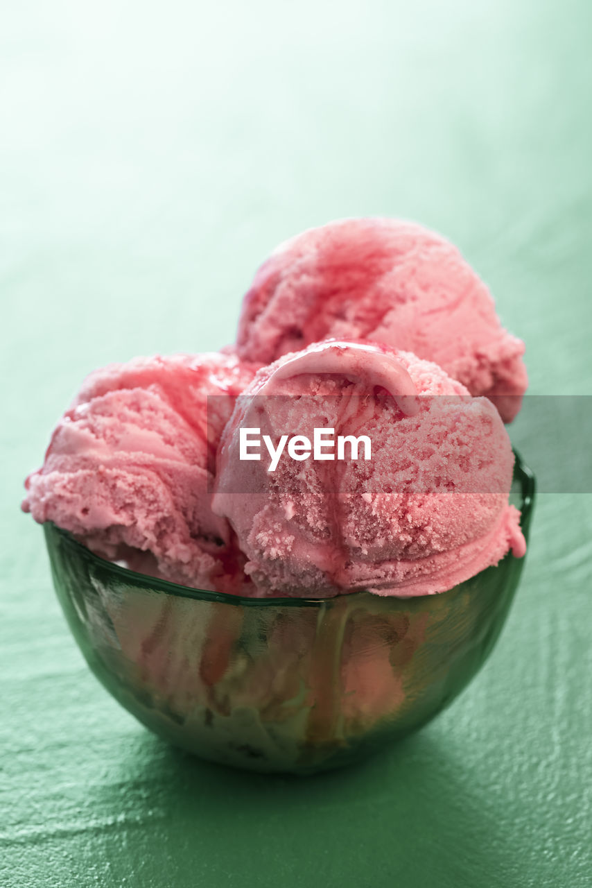 Strawberry ice cream bowl with a red topping, backlit,  on a green background. summer dessert.