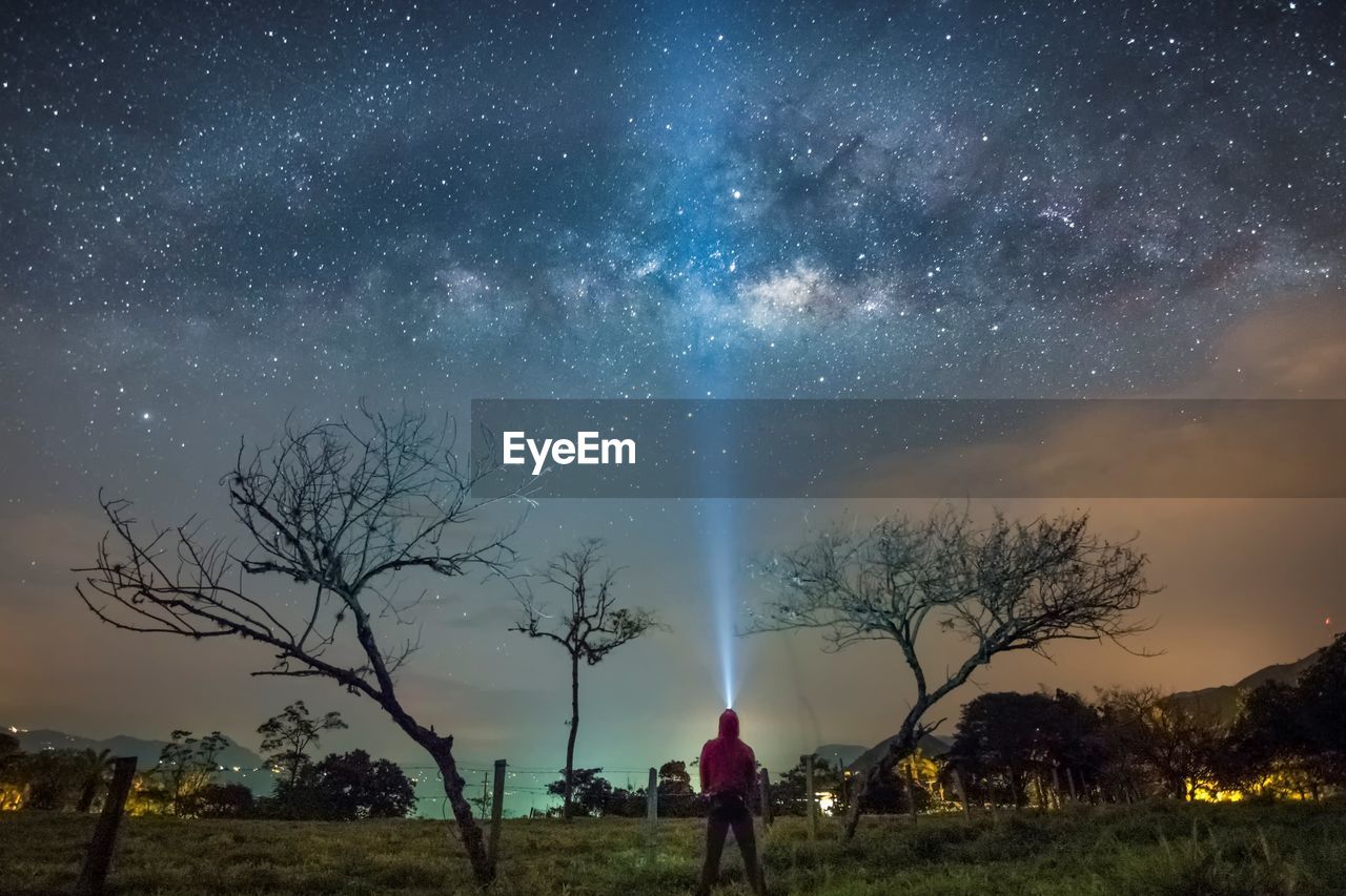 Man with illuminated headlamp standing on field against milky way