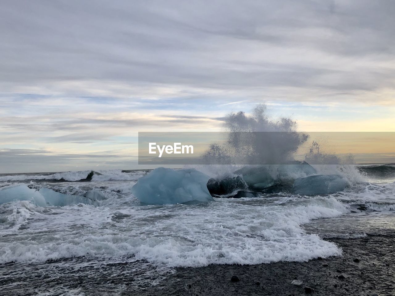 Sea waves splashing on ice against sky