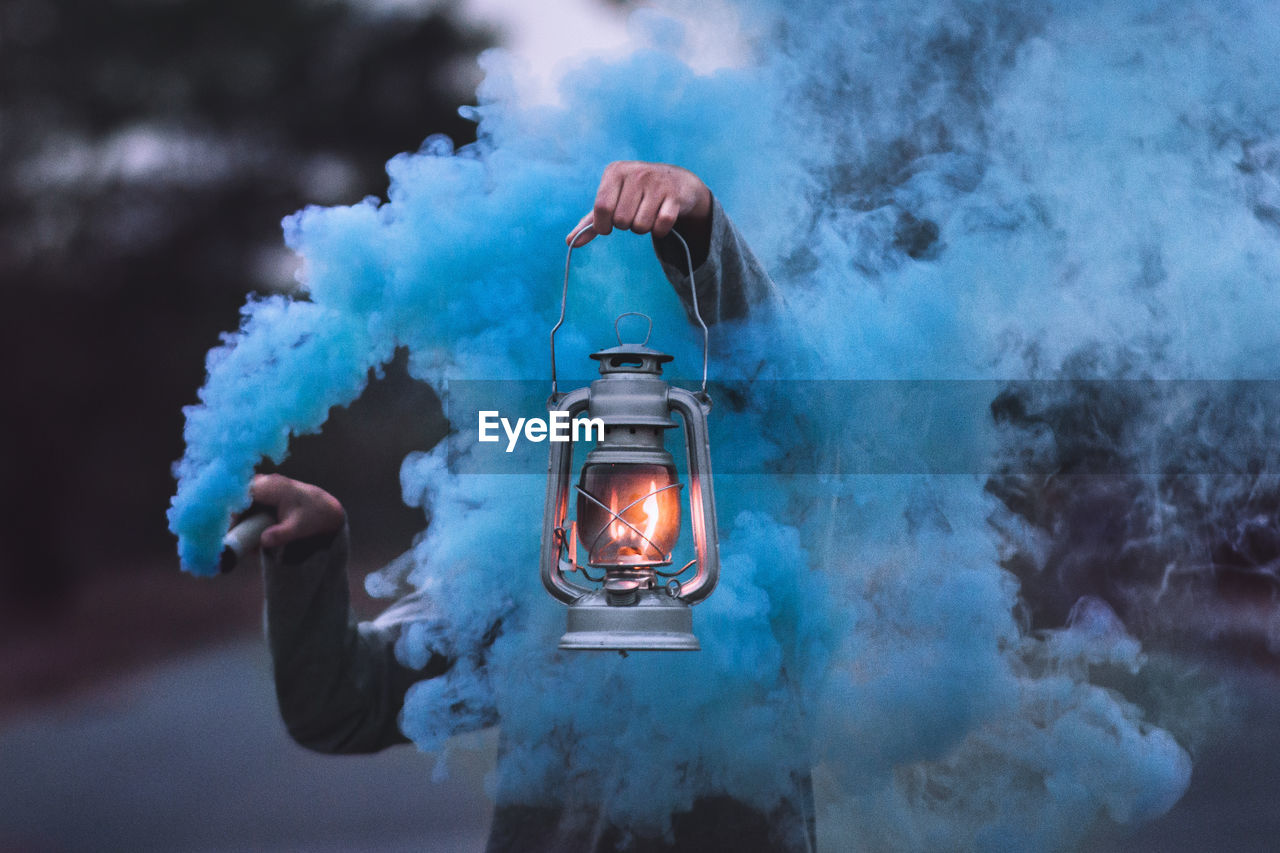 Person holding illuminated lantern amidst blue smoke