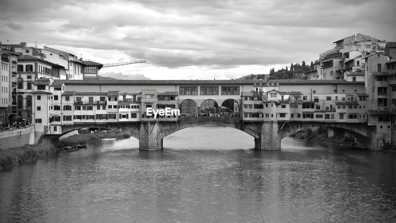 Bridge over river by buildings against sky