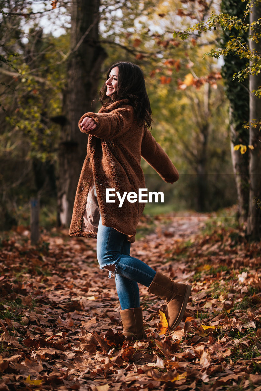 Woman dancing happily on a path covered with dry leaves.