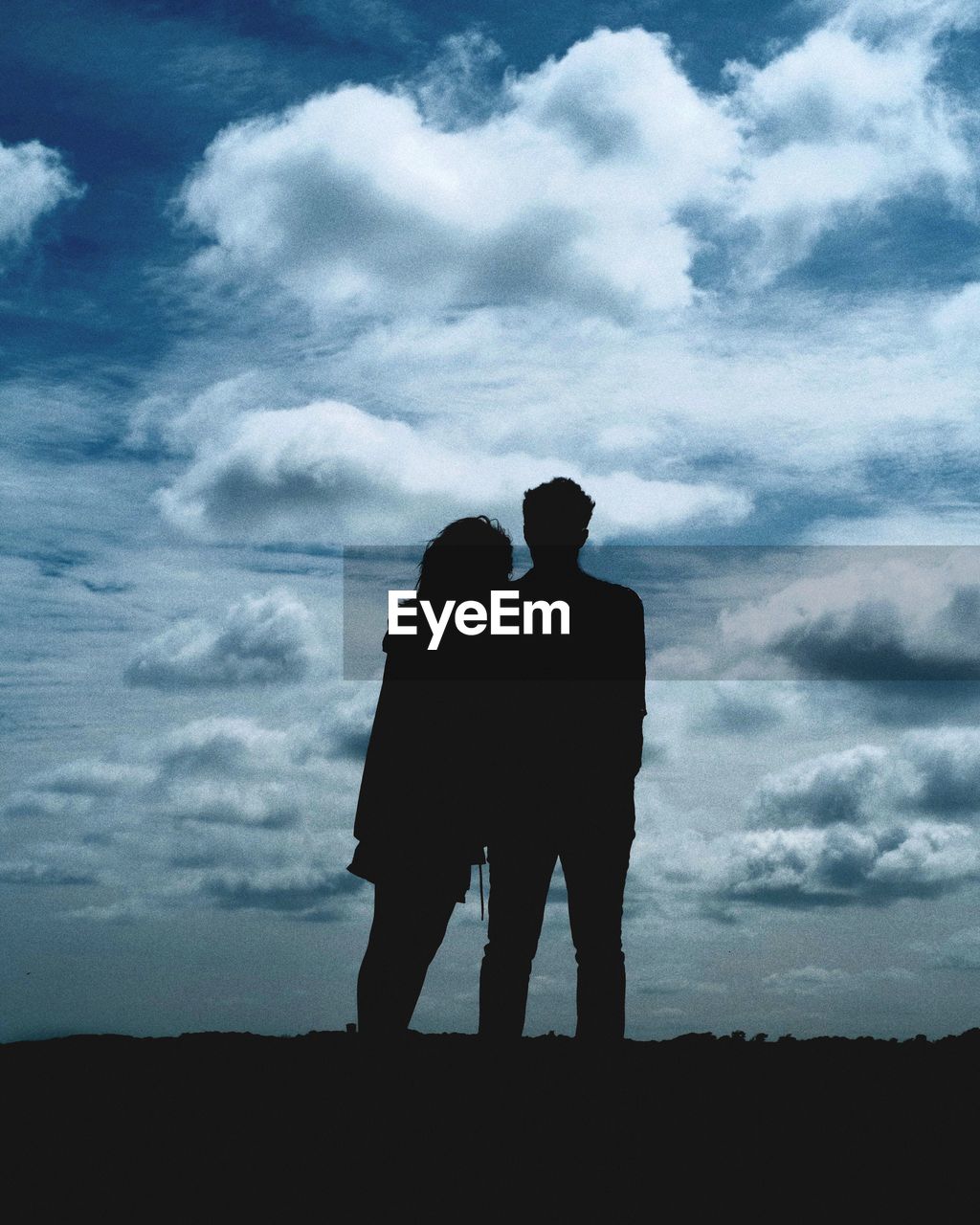 Low angle view of silhouette couple standing in field against sky during sunset