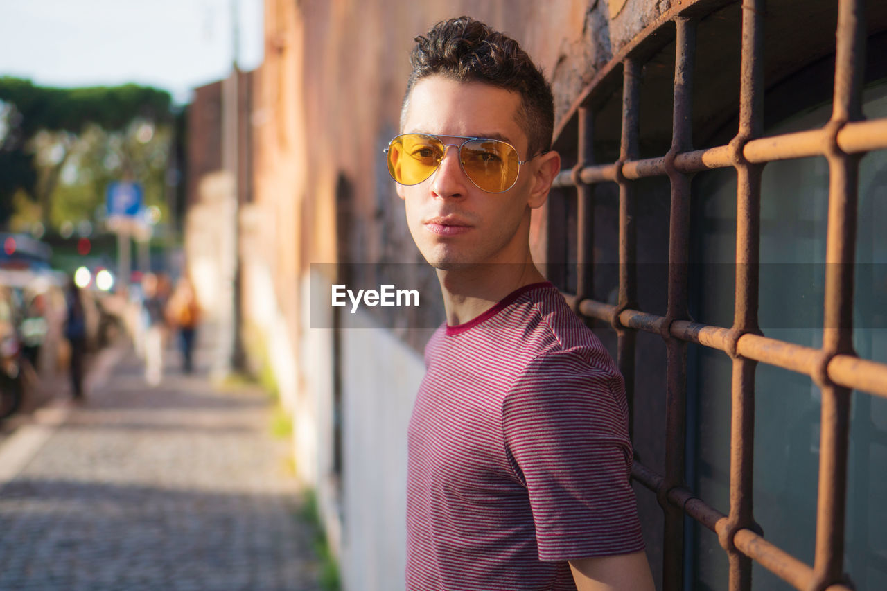 Portrait of young man wearing sunglasses while standing against wall