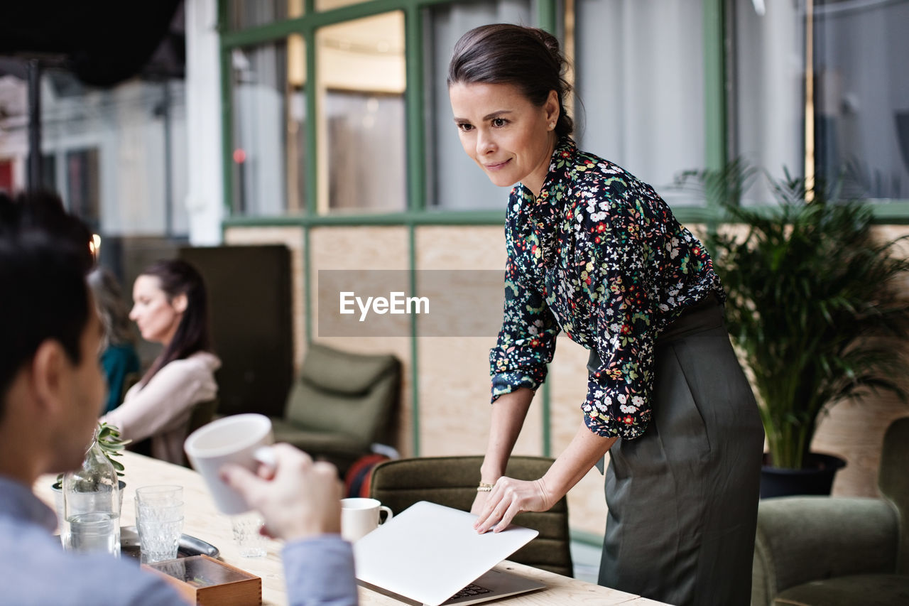 Businesswoman holding laptop while looking at coworker in office