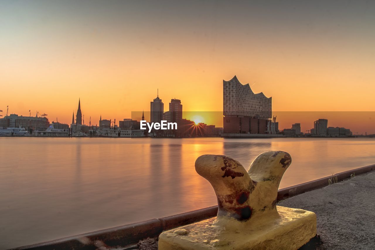 River by buildings against sky during sunset in city