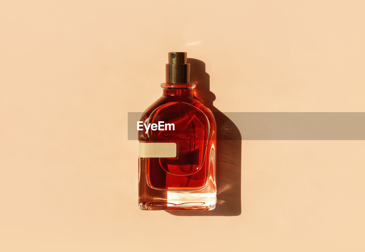 Transparent perfume bottle with red filling on a pastel beige background in the sunlight. flat lay