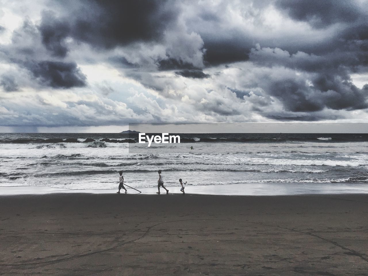 Children playing on beach by sea against cloudy sky