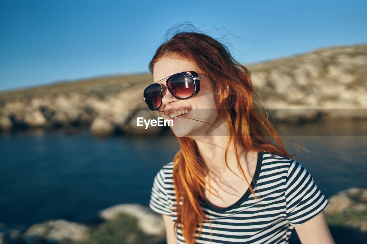 PORTRAIT OF WOMAN WEARING SUNGLASSES AGAINST SKY