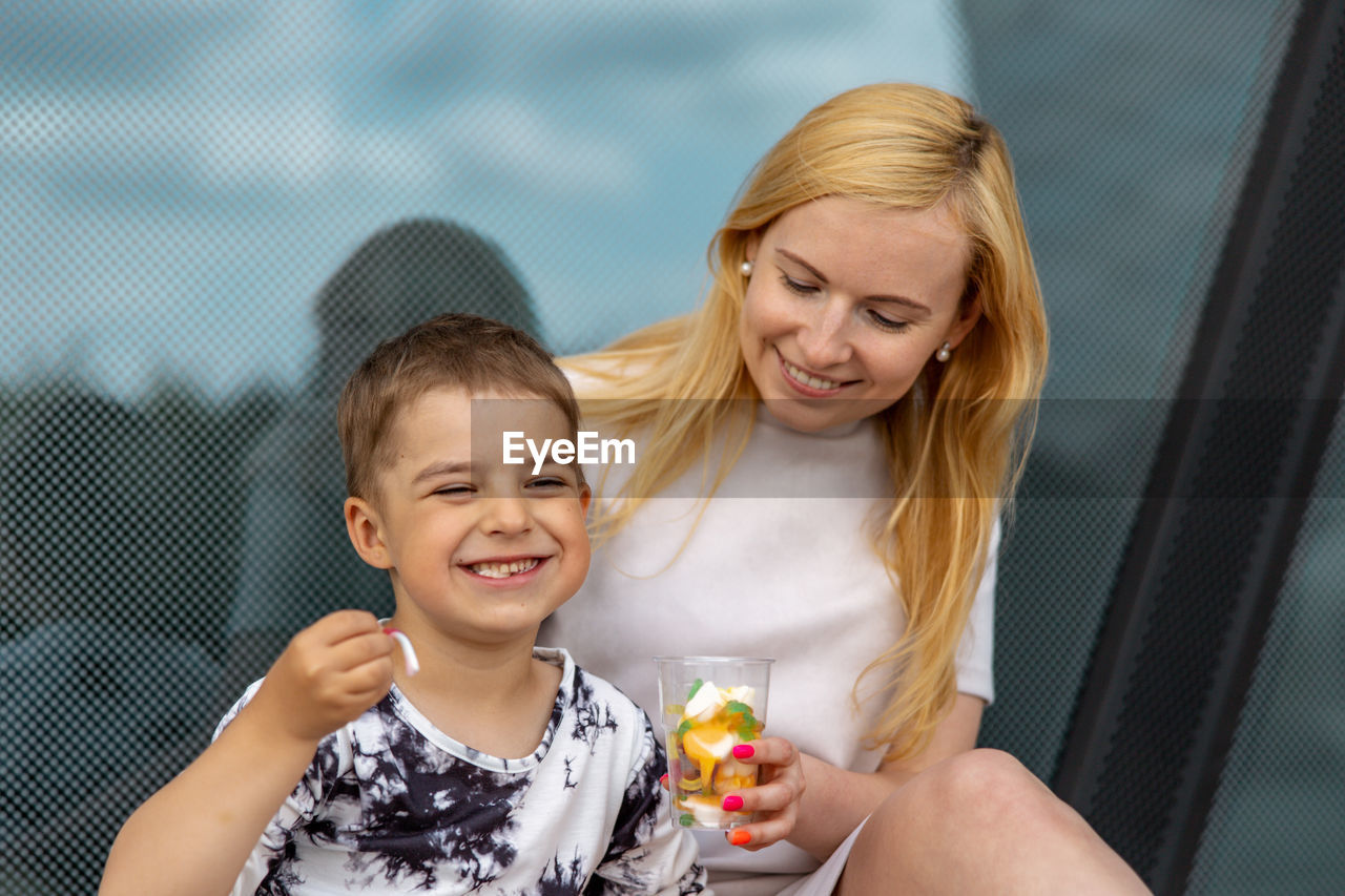 Happy blond woman and little boy sitting on terrace and eating sweets. mother and son enjoy