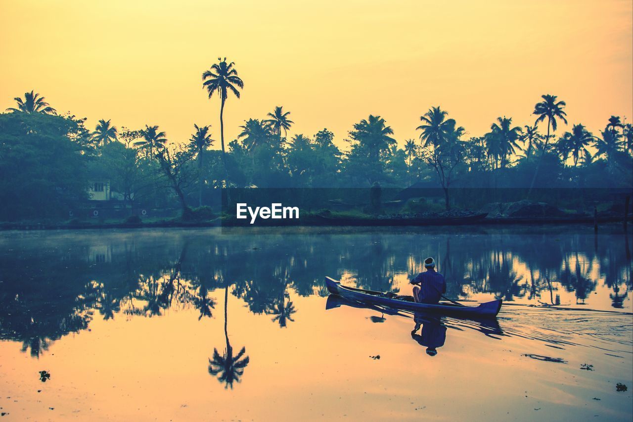 Man in boat sailing in river against sky during sunset