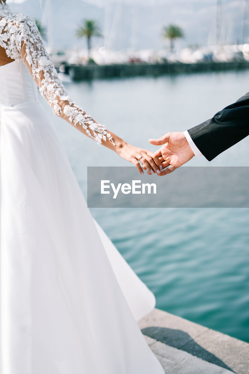 low section of bride and bridegroom holding hands