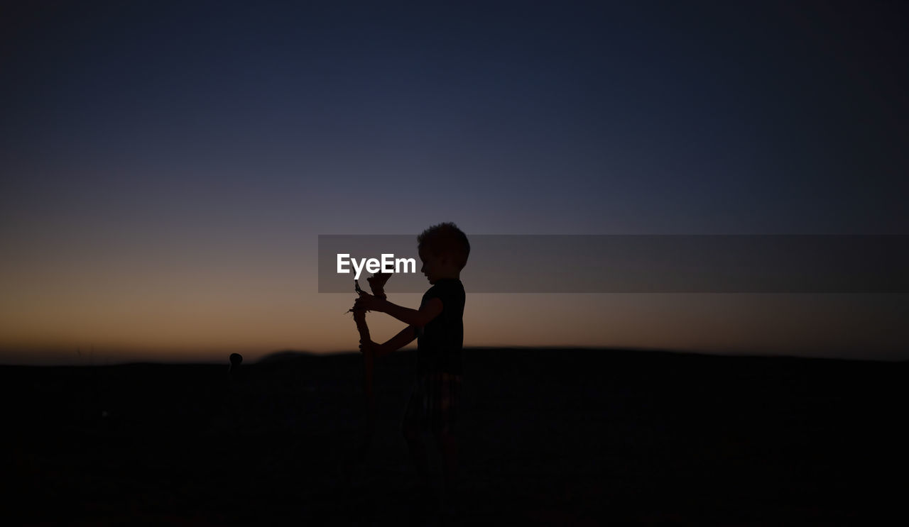 Silhouette of child standing against sky during sunset