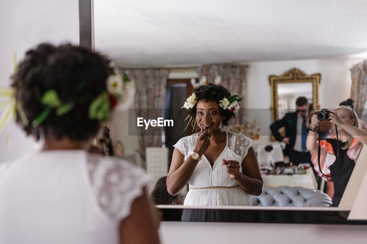 Reflection of bride applying lipstick while standing in front of mirror