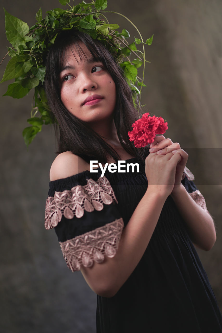 PORTRAIT OF BEAUTIFUL WOMAN WEARING RED ROSE STANDING AT HOME