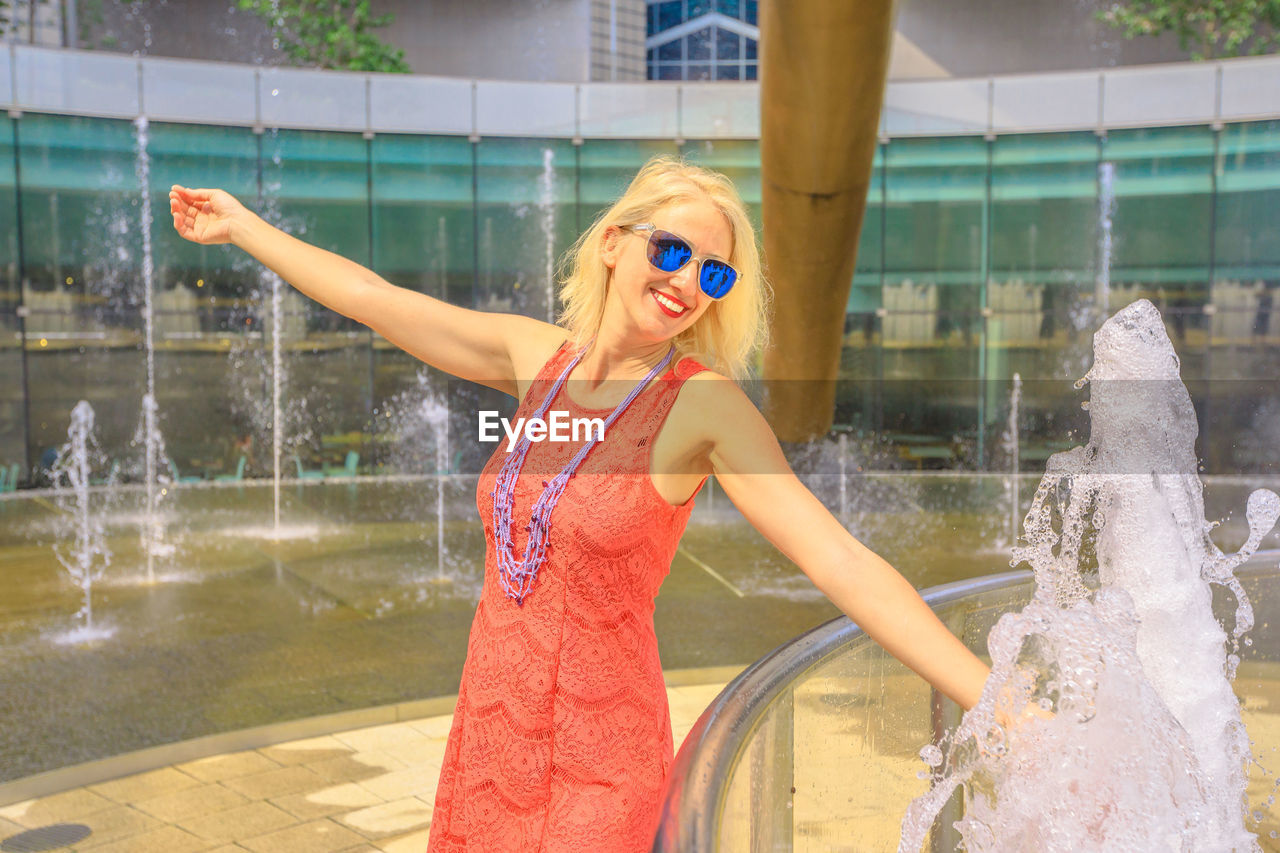 Smiling woman wearing sunglasses while standing by fountain