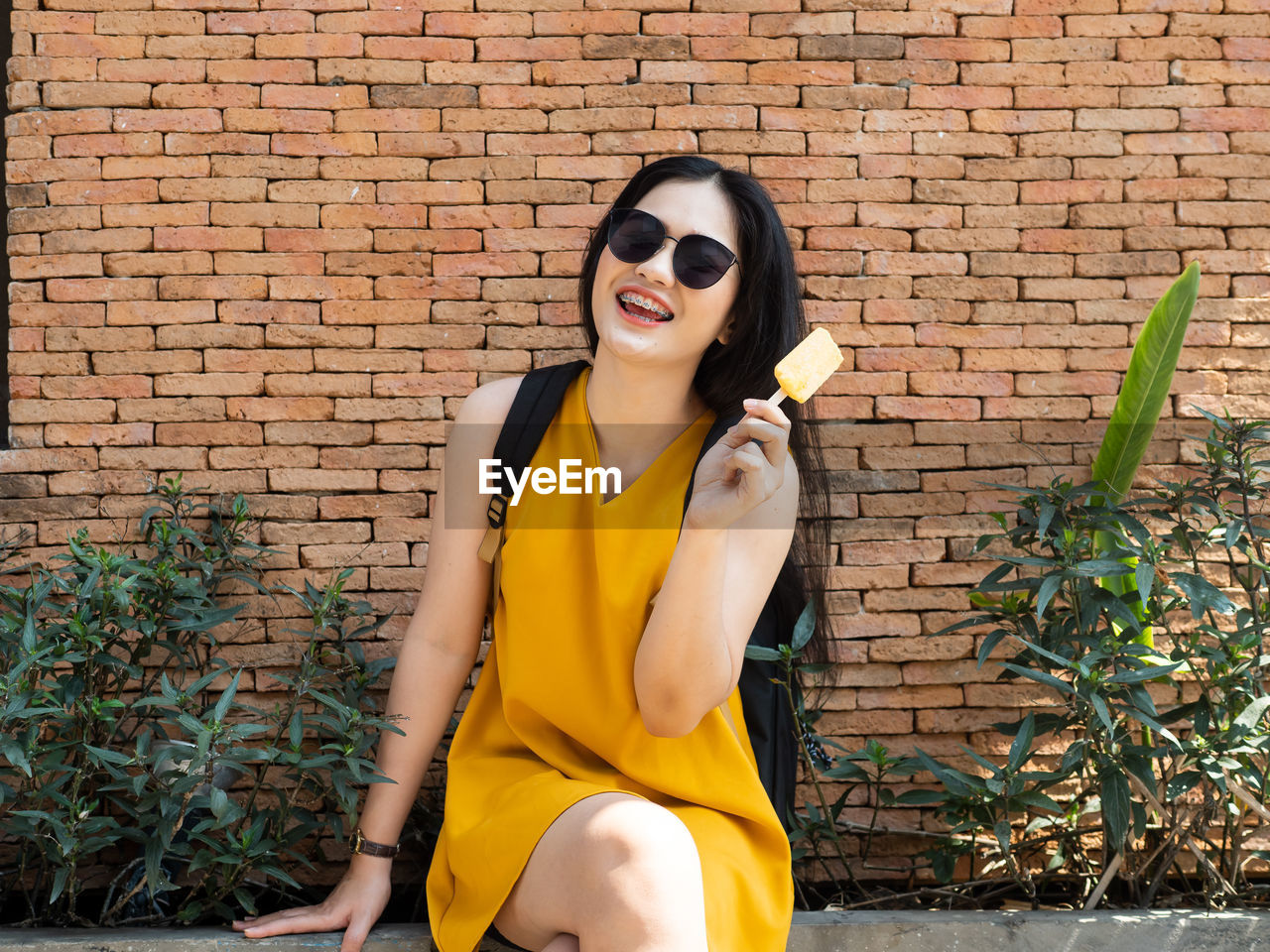 Young woman holding ice cream while standing against wall