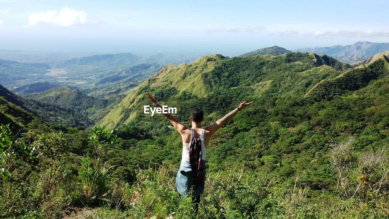 Rear view of young man with arms raised standing on mountain