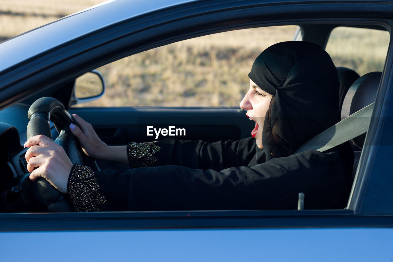Side view of woman wearing hijab driving car seen through window