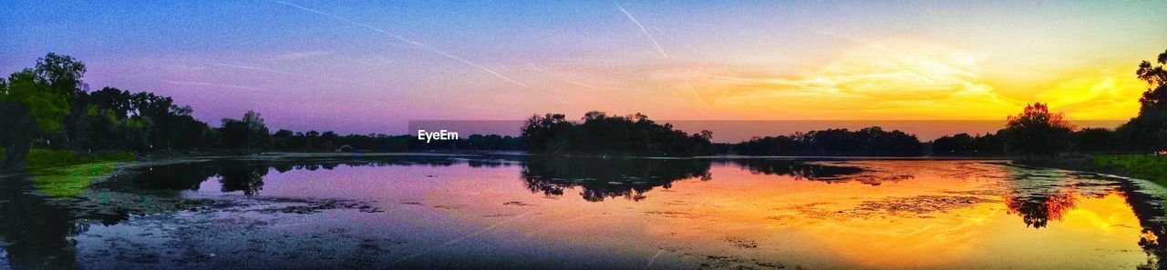 REFLECTION OF TREES IN WATER AT SUNSET