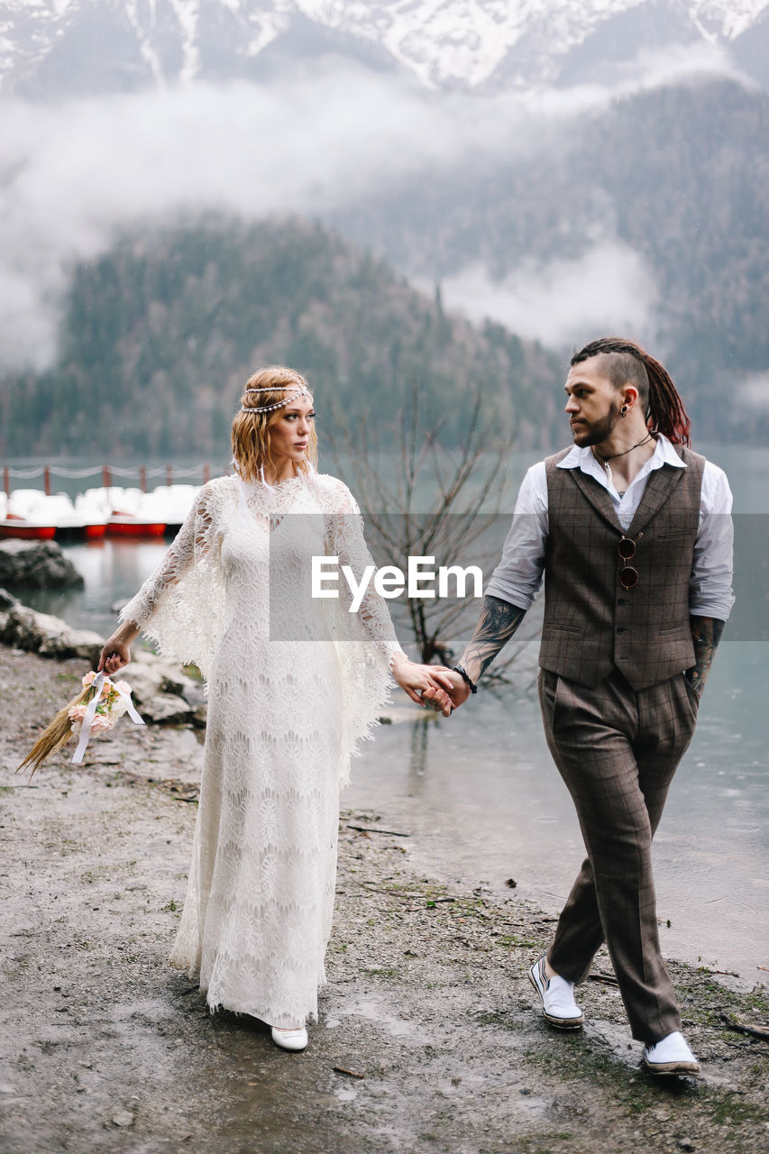 Happy newlyweds in love a man and a woman in wedding clothes embrace on the shore of the lake