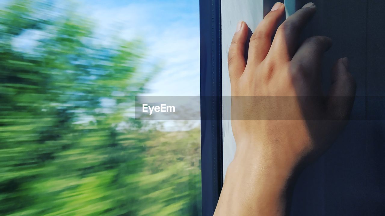 Cropped hand of person by window in moving train
