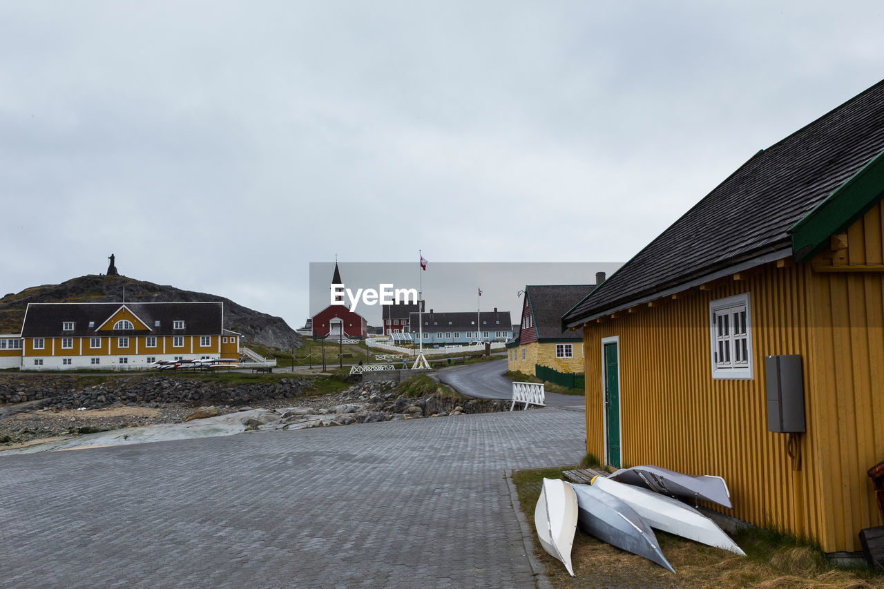 Grey and white kayaks resting against mustard colored house in the old part of nuuk, greenland,