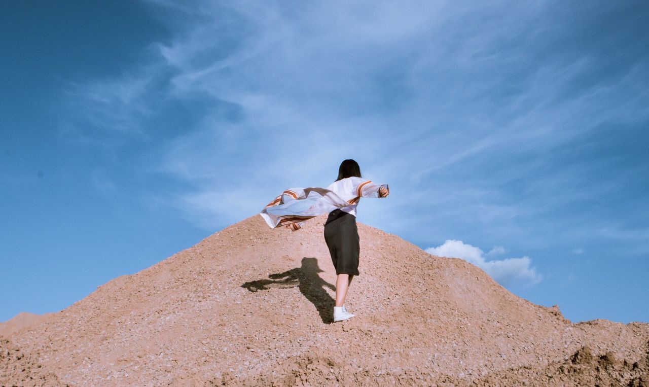 Low angle view of woman standing on mountain against sky