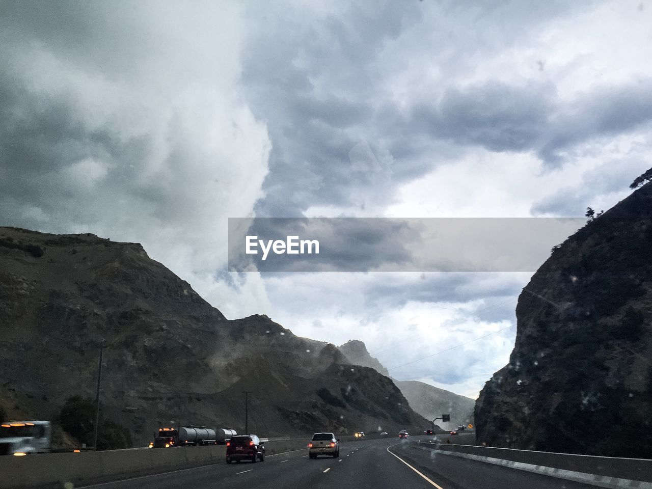ROAD PASSING THROUGH MOUNTAINS AGAINST CLOUDY SKY