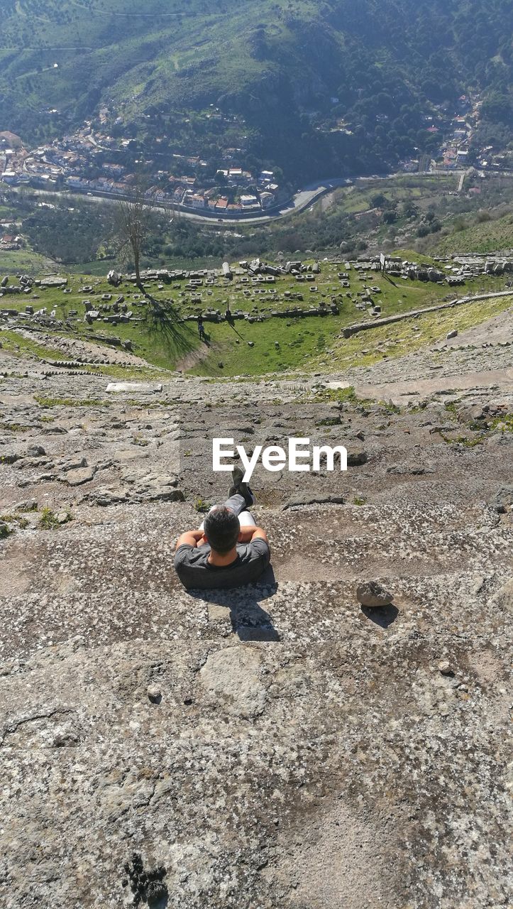 HIGH ANGLE VIEW OF PERSON SITTING ON ROCK