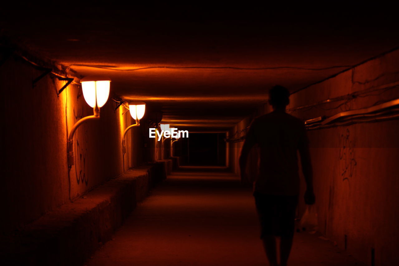 Rear view of silhouette man walking in illuminated tunnel at night