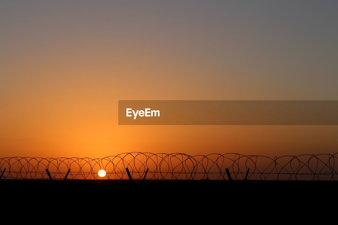 Razor wire fence against sky during sunset