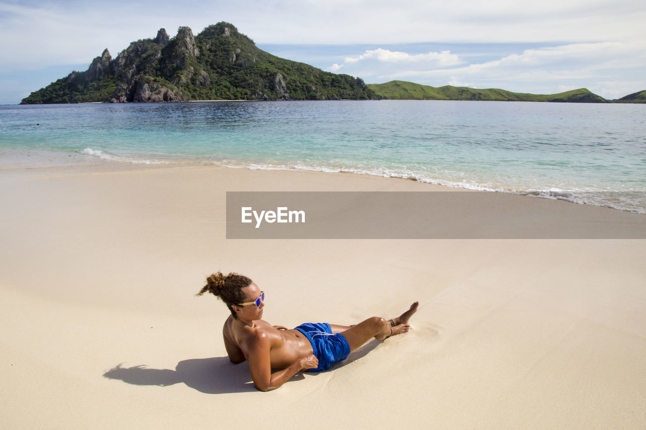 One male tourist, wearing blue swuimsuits, chilling on idyllic beach