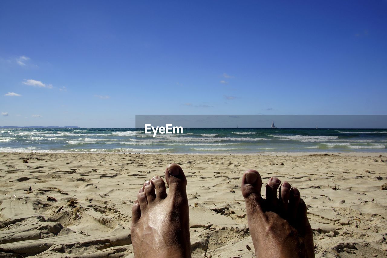 Low section of person at beach against sky