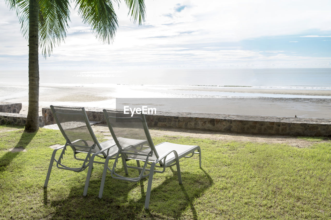 EMPTY CHAIR ON SHORE AT BEACH AGAINST SKY