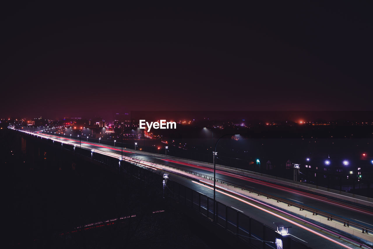 LIGHT TRAILS ON CITY STREET AGAINST SKY AT NIGHT