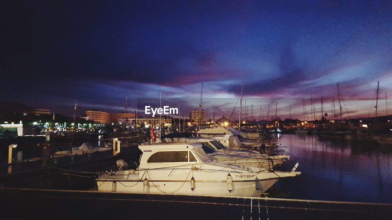 BOATS MOORED AT ILLUMINATED CITY AGAINST SKY