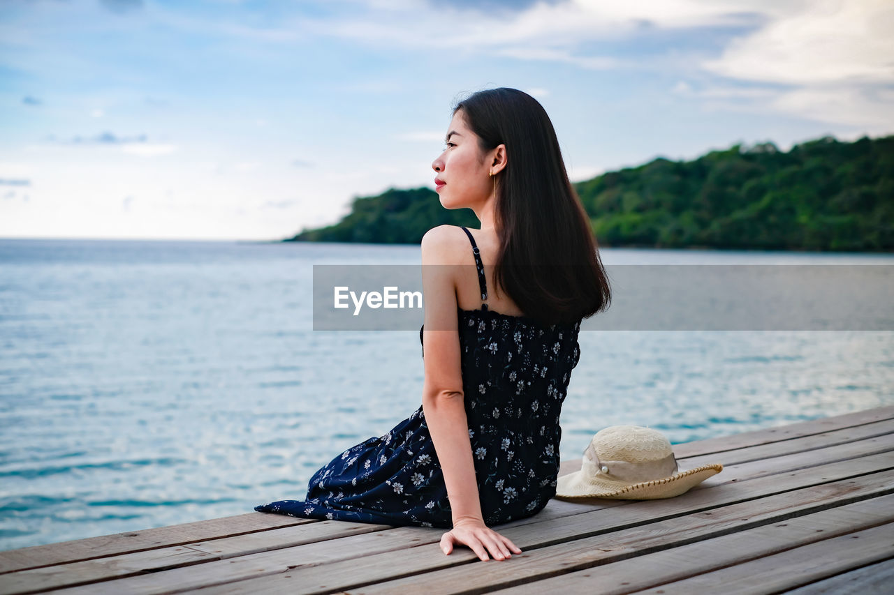 Young woman sitting on pier over sea against sky