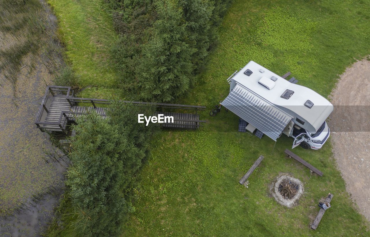 Aerial view of person sitting near camper van and wooden footbridge by lake