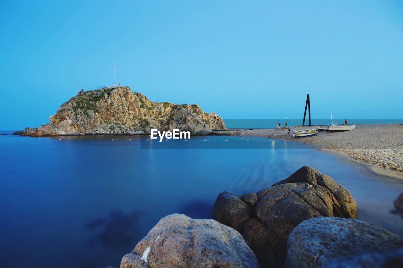 Rocks by seascape against clear blue sky