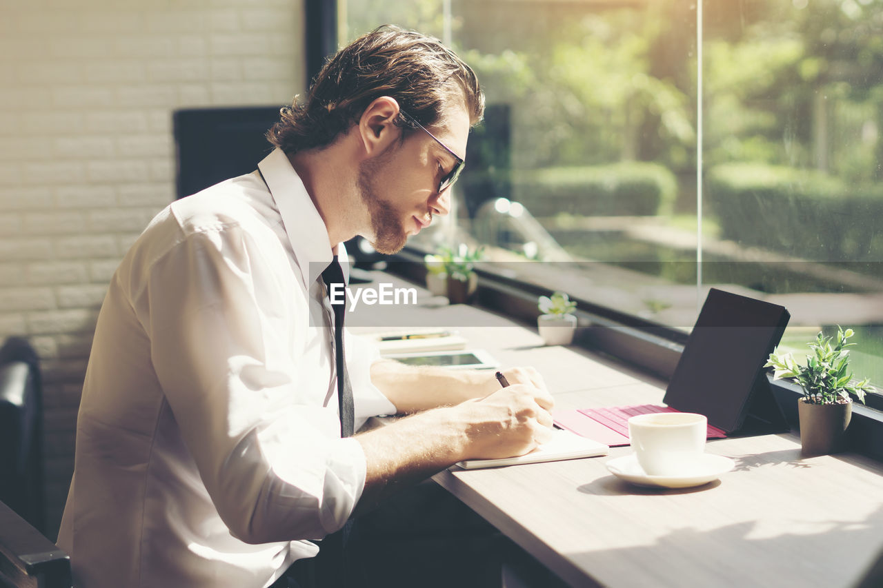 Businessman writing in book while sitting at desk in office