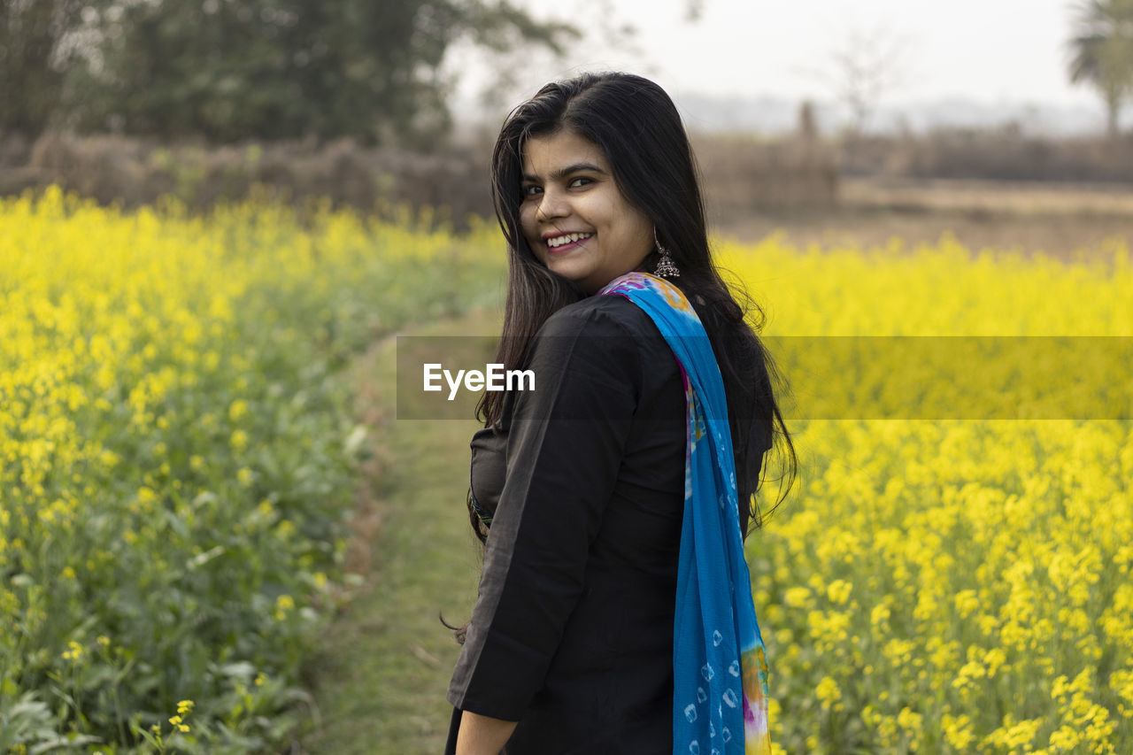 A pretty indian woman with smiling face looking back in mustard field with hair all over face