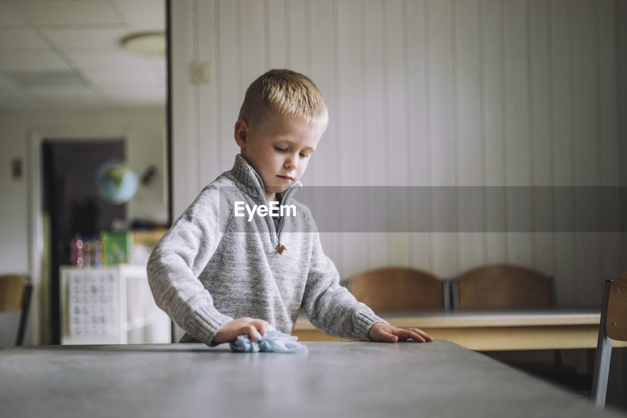 Boy cleaning dining table with napkin at day care center