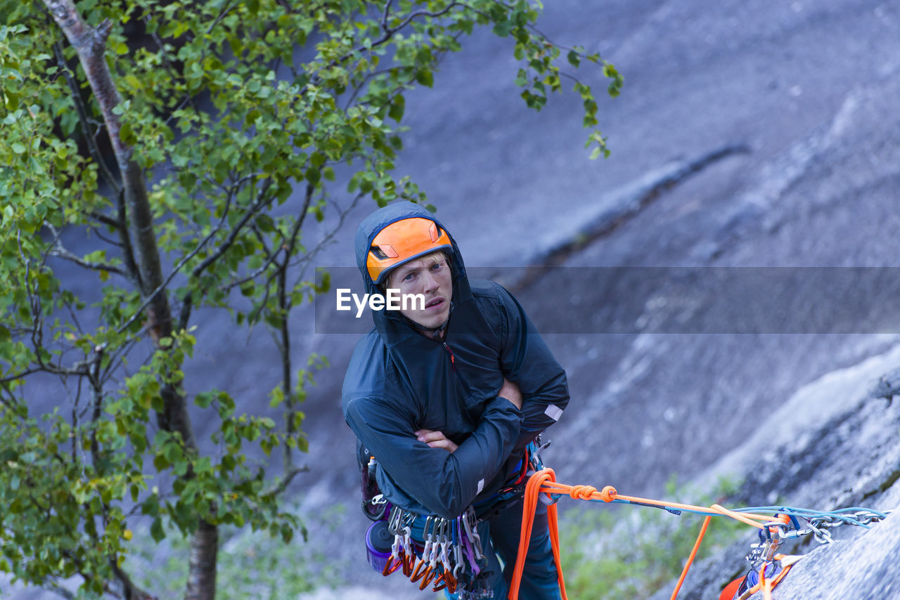 Man being bored belaying climber while hanging from granite wall cold