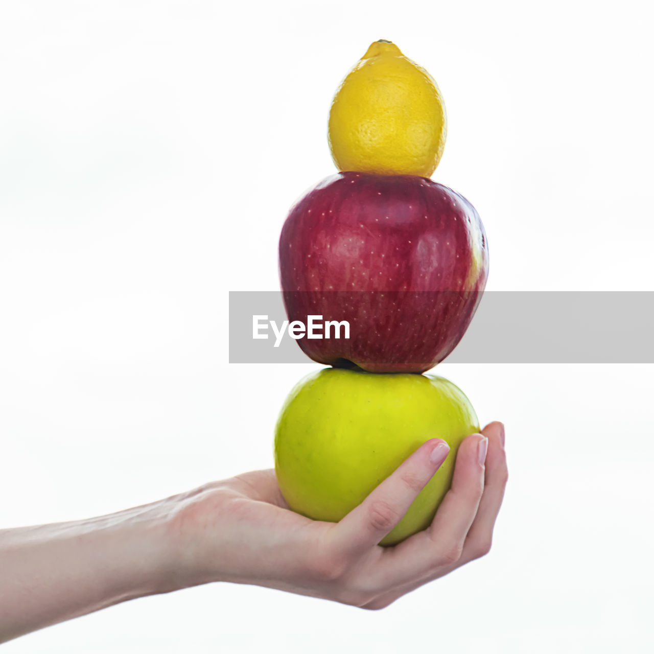 CLOSE-UP OF HAND HOLDING FRUITS OVER WHITE BACKGROUND