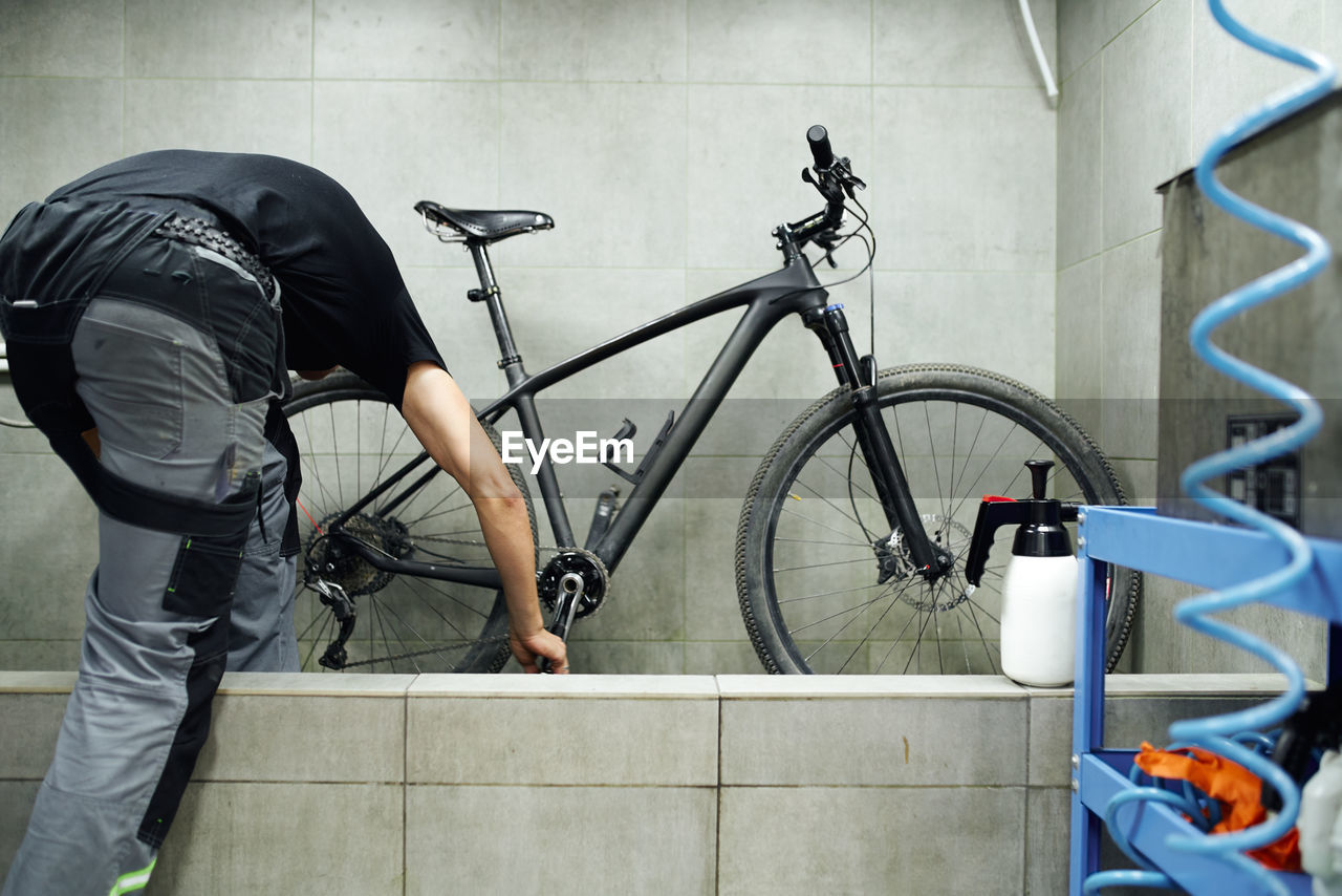 Unrecognizable male mechanic cleaning gear cassette of bicycle wheel with water in workshop