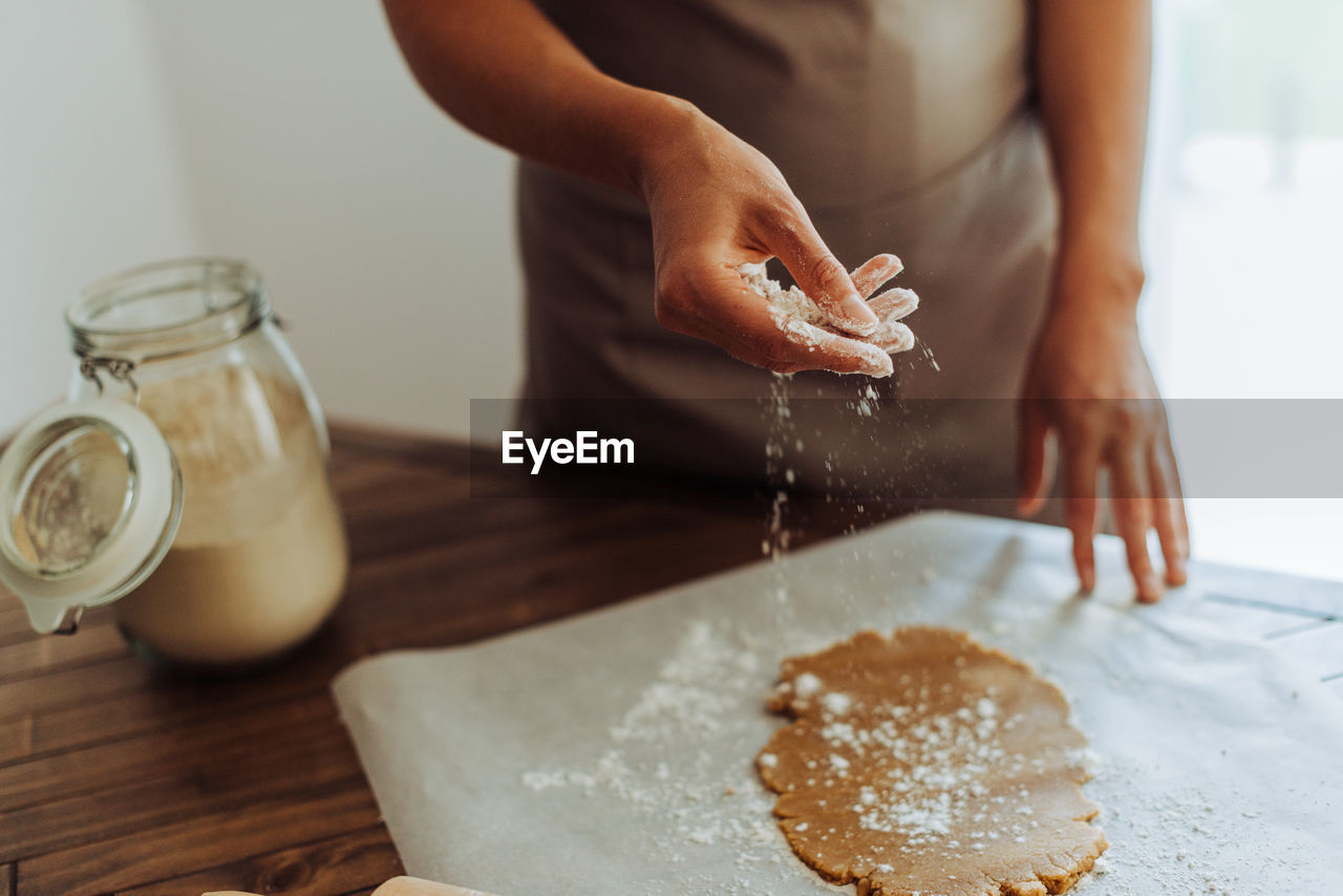 Midsection of a woman sprinkling dough with flour before rolling