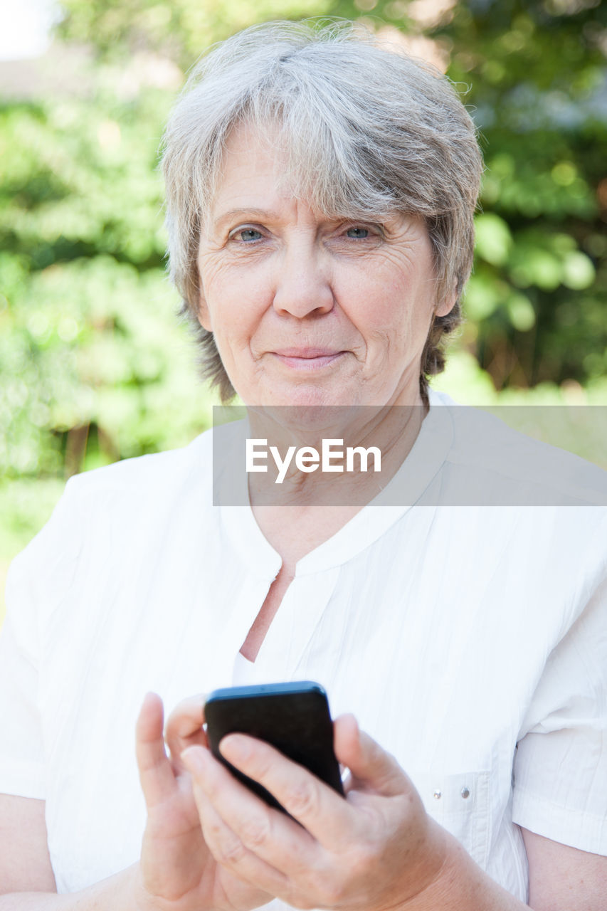 Portrait of senior woman using phone at park