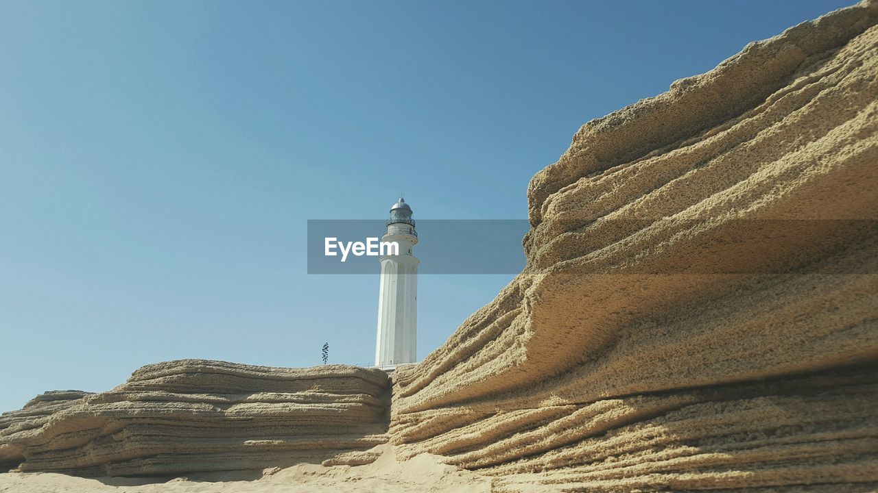 Low angle view of lighthouse on rock formation against clear sky